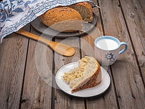 A slice of homemade bread on a light plate, a mug of milk, in the background bread with a slit