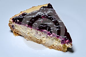 slice of homemade cheesecake covered with blueberry jam on a white plate