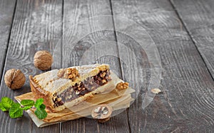 Slice of homemade hazelnut cake on a dark vintage wooden background. Near walnuts and a sprig of mint. Close-up Copy Space