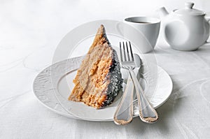 A slice of homemade multilayer biscuit cake. Soaked in butter. Served with chocolate icing and coconut. On a white plate is a fork