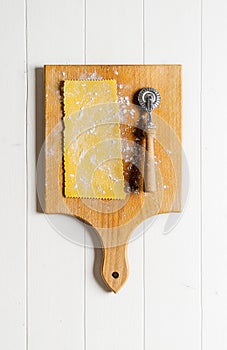 Slice of homemade pasta with cutter wheel on cutting board on wooden background