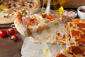 Slice of hot pizza with melting cheese and chorizo on rustic wooden table with ingredients