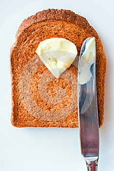 Slice of hot toast with melting butter and knife on a white plate