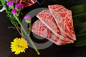 Slice Japanese beef neck chuck or jyu rosu wagyu serving on black plate and decorate with flower. Preparation for BBQ