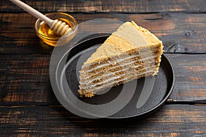 Slice of layered honey cake on dark wooden background