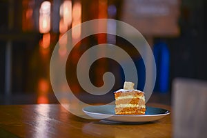 Slice of layered vanilla honey cake served on a blue plate on rustic wooden table over blurred restaurant background.