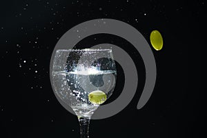 a slice of lemon falling into a glass cup with clear water causing splashes. Isolated on dark background