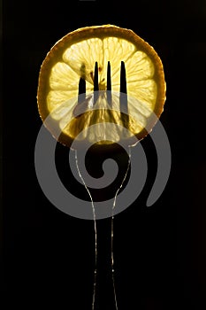 Slice of lemon on the fork on dark black background. silhouette of a fork in the back light