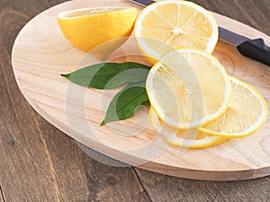 Slice lemon fruit with leaves and knife on cutting board.