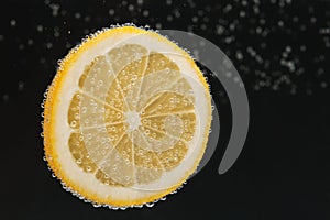 Slice of lemon in sparkling water on black background, space for text. Citrus soda