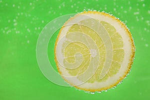 Slice of lemon in sparkling water on green background, space for text. Citrus soda