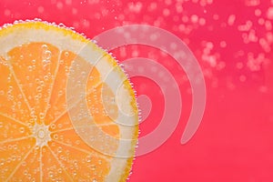 Slice of lemon in sparkling water on pink background, closeup with space for text. Citrus soda