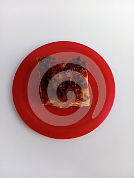 A slice of meat and cheese lasagne on a red plate on a white background