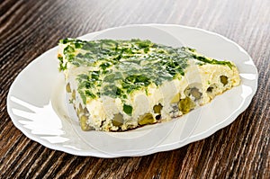 Slice of omelet with parsley and green peas in plate on wooden table