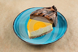 A slice of orange cheesecake and a slice of chocolate cheesecake on a blue plate.