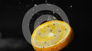 Slice of orange falls into the water with bubbles, splashes and foam on a black background