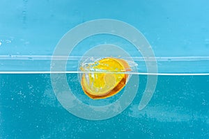 Slice of orange under water with transparent bubbles and water drops splashes. Cocktail making concept. Orange in pure