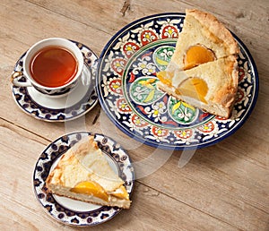 Slice of peach apricot pie or cheese sour cream cake on bright saucer with tea cup on wooden table