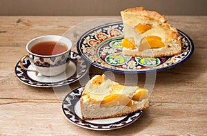 Slice of peach apricot pie or cheese sour cream cake on bright saucer with tea cup on wooden table