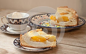 Slice of peach apricot pie or cheese sour cream cake on bright saucer with tea cup on wooden table