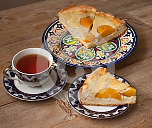 Slice of peach apricot pie or cheese sour cream cake on bright saucer with tea cup on wooden table