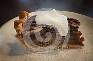 A slice of pecan pie with whipped cream on a white plate,Traditional Thanksgiving individual serving of pecan pie on  table and
