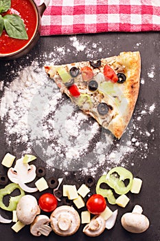 Slice of pizza vegetariana on table with flour, tomatoes, mushrooms, olives photo