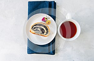 Slice of poppy seed roll served on a plate and a cup of tea on a
