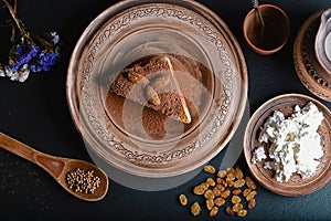 Slice of poured honey cake with cheese cream on a clay vintage plate, decorated with cocoa and almonds, wooden spoon with cardamom