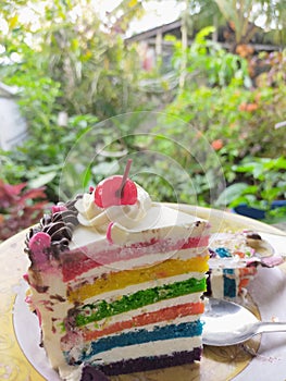 A slice of rainbow cake with a Cherry on top