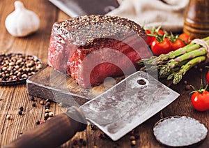 Slice of Raw Beef Topside Joint with Salt and Pepper on wooden chopping board with meat hatchet, garlic and asparagus tips photo