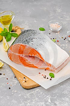 Slice of red fish salmon with lemon, olive oil, fresh basil and spice on a wooden board on a gray background. Copy space