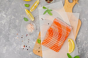 Slice of red fish salmon with lemon, olive oil, fresh basil and spice on a wooden board on a gray background. Copy space