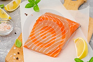 Slice of red fish salmon with lemon, olive oil, fresh basil and spice on a wooden board on a gray background. Copy space