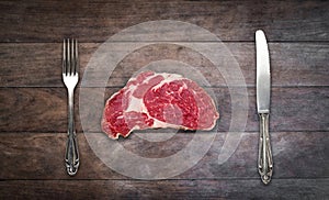 Slice red meat / raw steak with knife and fork on wooden background