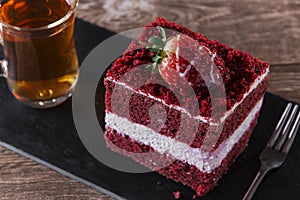 slice of red velvet cake with white frosting is garnished with strawberries close up