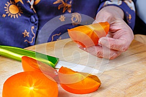 Slice of ripe bright orange juicy persimmon in the elderly woman hand