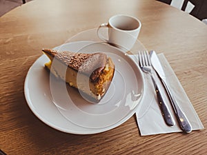 A slice of San Sebastian Cheesecake on a plate with a coffee in a cafe