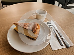 A slice of San Sebastian Cheesecake on a plate with a coffee in a cafe