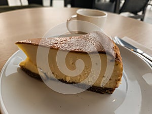 A slice of San Sebastian Cheesecake on a plate with a coffee in a cafe