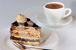 Slice of sponge cake with chocolate icing and cup of coffee on white background. Delicious dessert. Closeup