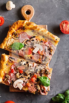 Slice of square pizza with basil tomatoes and mushrooms on a wooden board