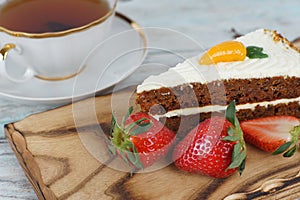 A slice of sweet carrot cake and a mug of tea next to red strawberries