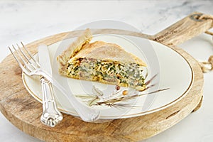 Slice of Swiss pie with chard, rice, onions and pine nuts in plate on wooden stand on white marble