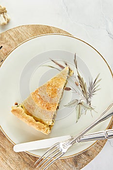 Slice of Swiss pie with chard, rice, onions and pine nuts in plate on wooden stand on white marble