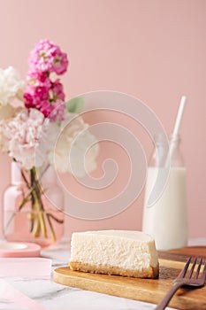 Slice of tasty homemade cheesecake with flowers and miilk on pink background. Healthy organic summer dessert pie.