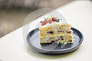 A slice of Vanilla Mixed Berry Cake adorned with mulberries on top, revealing the layers of mixed berries and cream, as well as