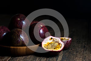 Slice and whole passion fruits in a wooden tray on a rustic wooden table.