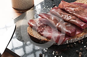 Slice of wholemeal bread with bresaola dried beef on a black granite cutting board. Bresaola is a famous Italian salami with