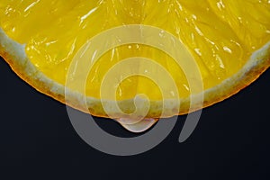 Slice of yellow lemon with juice drops on a black background, macro photography. Texture fresh citrus fruit, closeup